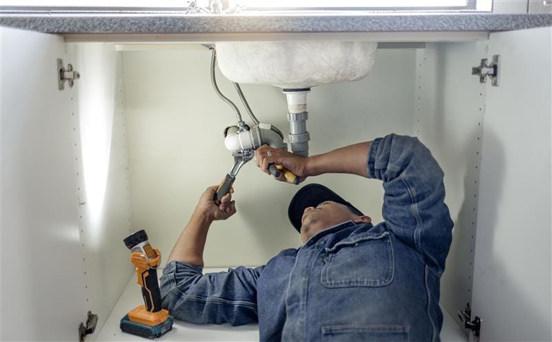 Plumber repairing pipes beneath a bathroom sink in Stockton
